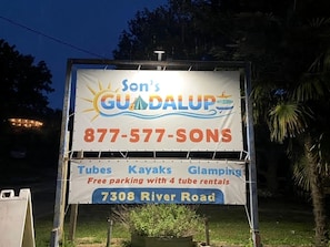 Schild für Son's GUDA LUPS mit der Kontaktnummer 877-577-SONS, das Schlauchboote, Kajaks und Glamping mit kostenlosem Parkplatz und 4 Schlauchbootverleihungen anbietet.