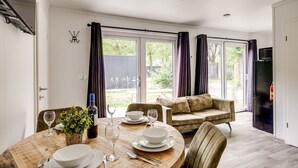 A dining area with a round table set for four, a sofa, and a refrigerator in the background.