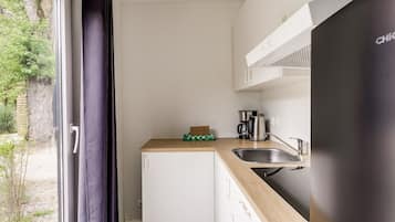 Een compacte keuken met een geïntegreerde koelkast, een koffiezetapparaat en een spoelbak.