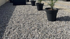 Un bâtiment avec un toit rouge et des éléments décoratifs blancs, une terrasse en gravier et des plantes en pot.