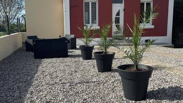 Un bâtiment avec un toit rouge et des éléments décoratifs blancs, une terrasse en gravier et des plantes en pot.