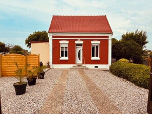 A red brick building with a white door, a small porch, and gravel driveway.