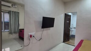Quarto de hotel com cama, televisão fixada na parede, espelho e banheiro visível por uma porta aberta.
