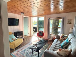 Ett mysigt vardagsrum med ett träpanelat tak, en soffa, en bänk, en tv och en röd fåtölj.