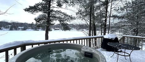 Un jacuzzi en una terraza con paisajes nevados y vistas a un lago.