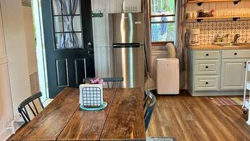 A compact kitchen with a wooden table, chairs, a refrigerator, a sink, and a window.