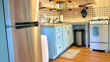 A kitchen with a stainless steel refrigerator, white cabinets, wooden shelves, a clock, and a stove.