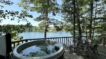A hot tub on a wooden deck with a view of a lake and trees.