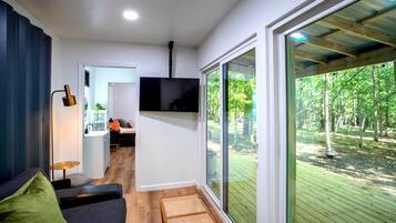 A modern interior with a sofa, a flat-screen TV, and a large sliding glass door leading to an outdoor deck.