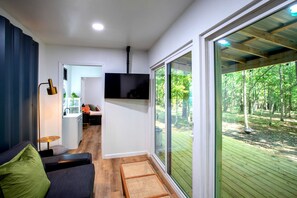 Un interior moderno con un sofá, un televisor de pantalla plana y un amplio ventanal corredero que da a una terraza exterior.