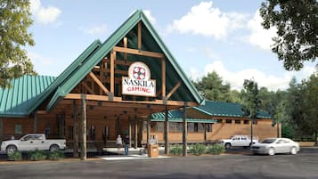 A log cabin-style building with a green roof, a sign reading 'NASKILA GAMING,' and a parking lot with cars.