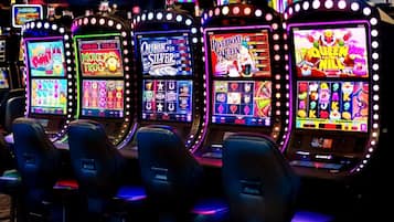 A row of slot machines with illuminated screens, each displaying different game themes.
