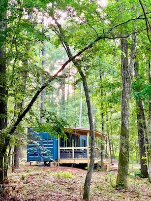 A cabin in a forest with a deck and a blue structure nearby.
