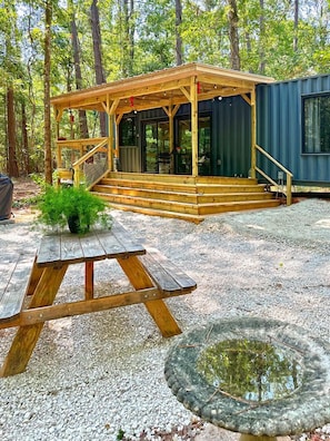 A wooden deck with a staircase leading to a covered area, a picnic table, and a small pond.
