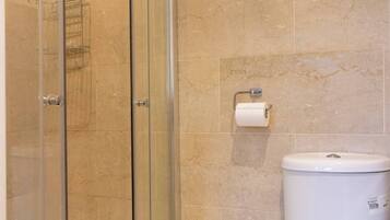 A bathroom with a glass-enclosed shower, a toilet, and a paper towel dispenser.