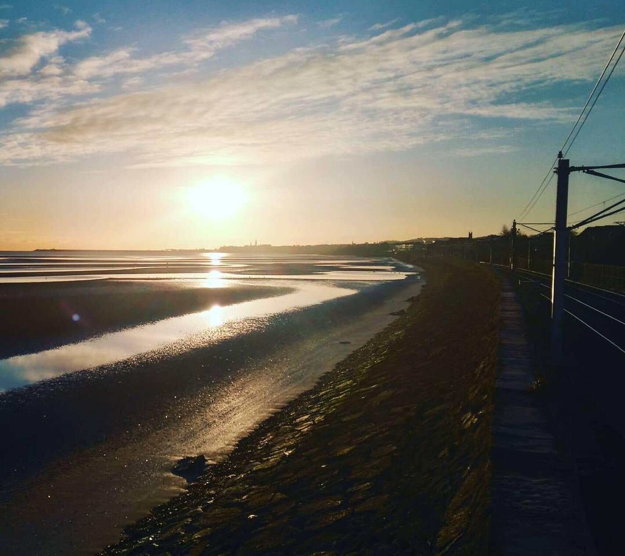 Eine Küstenlandschaft mit sonnigem Strand, einem Bahnweg und einer fernen Stadtlinie.