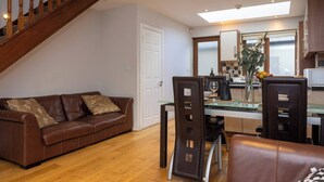 Uma sala de estar moderna com um sofá de couro marrom, uma mesa de jantar de vidro e uma escada.