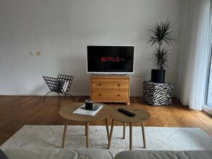 A living room with a TV, wooden furniture, a plant, and a zebra-patterned ottoman. - Hideaway in Strobl with bathing area and breakfast at partner hotel (Strobl)