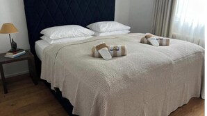 En pænt redt seng med en quiltet sengegavl, hvide puder og et foldet håndklæde på sengen.