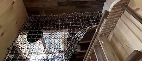 Una cabaña de madera con un entrepiso para dormir, una ventana que da a vistas de vegetación y un suelo de malla metálica.