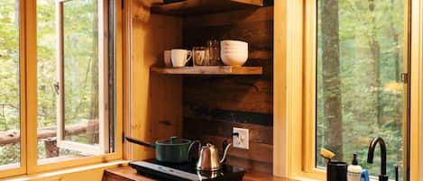 Une cuisine rustique aménagée dans une cabane en bois, avec une fenêtre, un évier, une cuisinière et des étagères remplies de vaisselle.