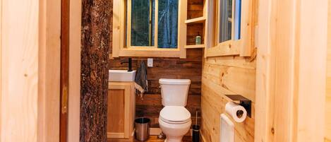 Un baño de madera pequeño y funcional con inodoro, lavabo y ventana.