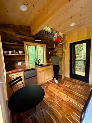 L’intérieur d’un chalet en bois comprend une cuisine, un coin repas et une grande fenêtre.