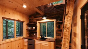 A wooden cabin kitchen with a refrigerator, sink, and windows overlooking a forest.