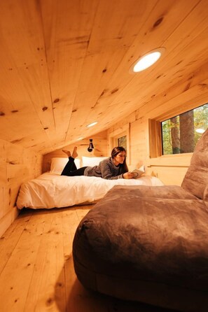 Une cabane en bois avec un lit, un fauteuil de lecture et une fenêtre.