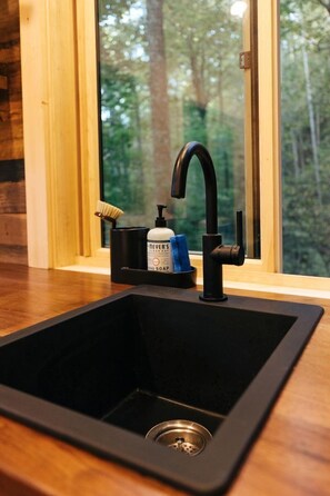 A modern kitchen sink with a black faucet, a soap dispenser, and a brush holder.