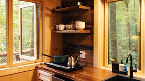 A wooden cabin kitchen with a window, a sink, a stove, and shelves with dishes.