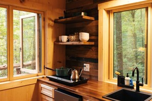 A wooden cabin kitchen with a window, a sink, a stove, and shelves with dishes.