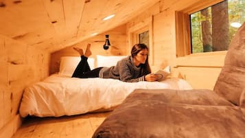 A wooden cabin with a bed, a reading chair, and a window.