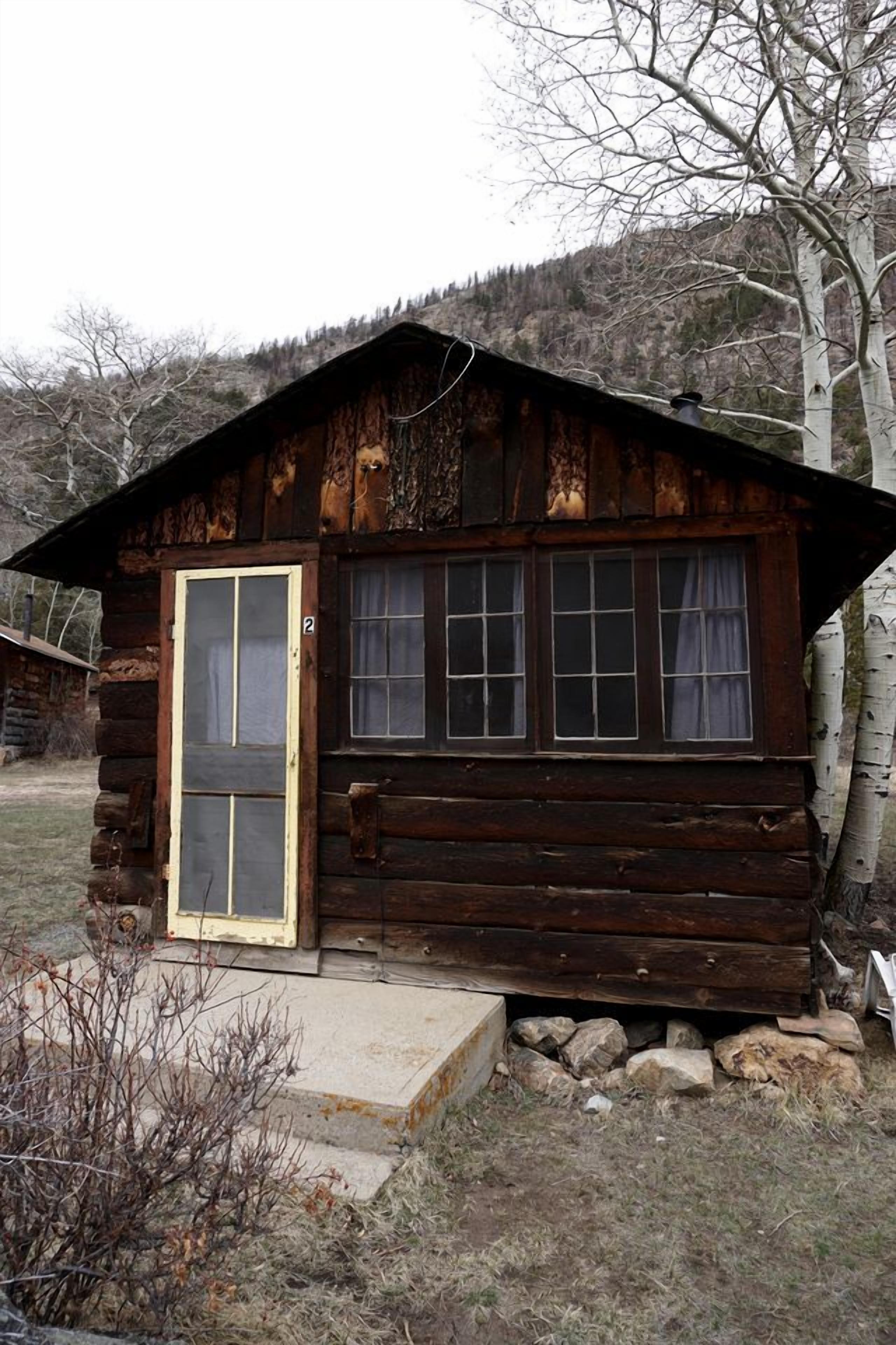 A rustic log cabin with a single door and windows, surrounded by a natural landscape.