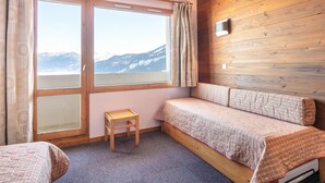 A room with a bed, a small wooden stool, and a window with a view of mountains. - Compact Alpine Stay for 3 in Doucy (La Léchère)