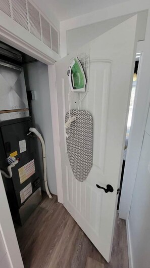A room with a white door, a small ironing board with an iron, and a heater unit.