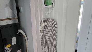 Una habitación con una puerta blanca, una plancha sobre un tendedero pequeño y un calentador.