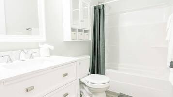 A bathroom with a white vanity, a toilet, a shower with a curtain, and a mirror above the vanity.