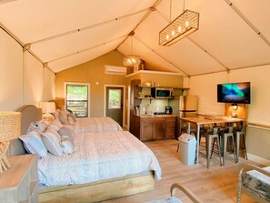 Eine Zeltunterkunft mit Bett, Küchenzeile, Essbereich und Fernseher.