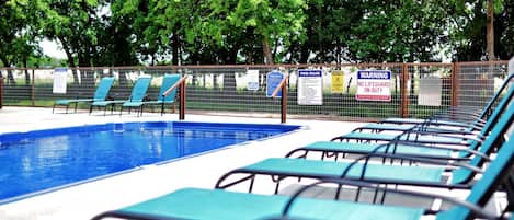 En swimmingpool med blått vatten, omgiven av ett staket och med solstolar runt omkring.