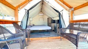 A tented accommodation with a bed, two wicker chairs, a small kitchenette, and a wooden deck. - C Son's Luxurious Safari Tent in Kingsbury, TX (Kingsbury)