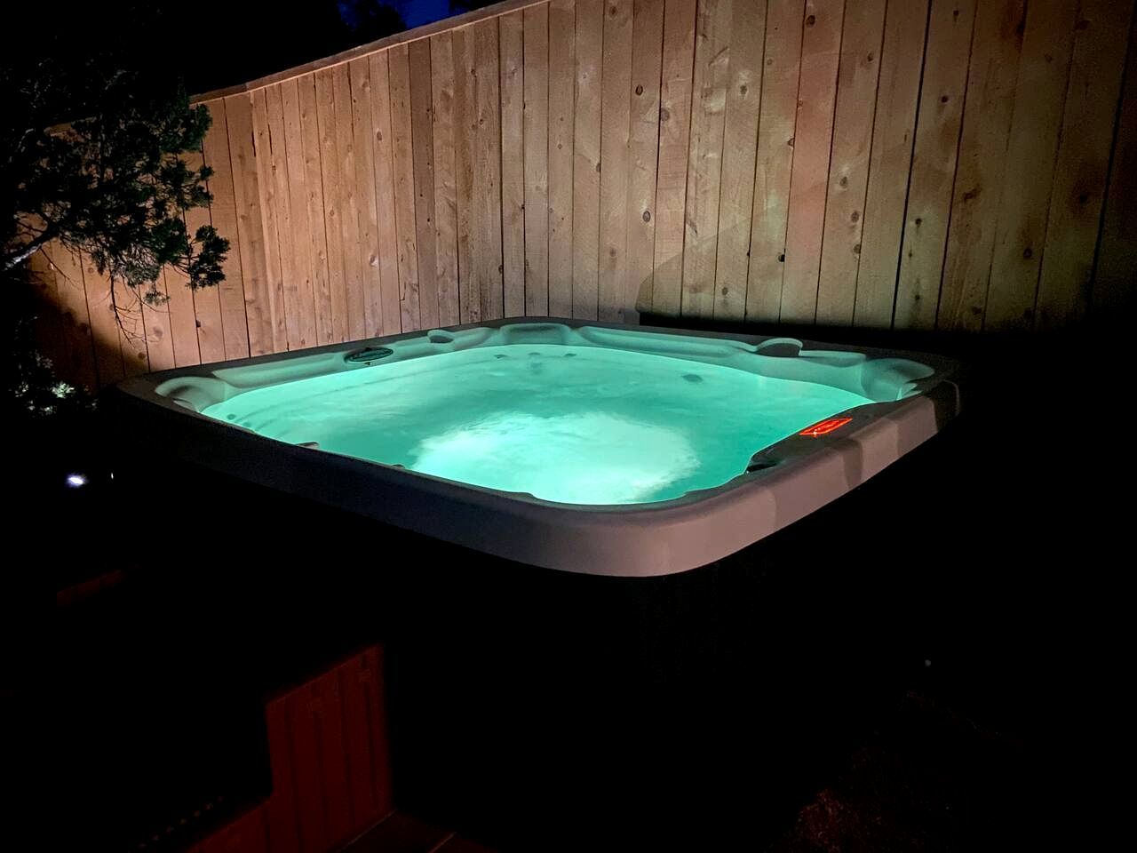 Un jacuzzi con terraza de madera y un árbol al fondo.