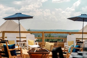 Une terrasse sur le toit, avec des chaises et des tables blanches, deux grands parasols et une vue sur le paysage.