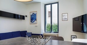 A modern dining area with a blue sofa, a dining table, and artwork on the walls. - Welcome to this modern, minimalist one-bedroom flat, perfect for a comfortable stay for two in pleasant surroundings. (Annecy)