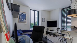 Ein modernes Wohnzimmer mit einer Couch, einem Glastisch, einem Fernseher und einem Essbereich mit einem Stuhl und einem kleinen Tisch.