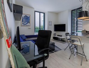 A modern living room with a sofa, a glass table, a TV, and a dining area with a chair and a small table. - Welcome to this modern, minimalist one-bedroom flat, perfect for a comfortable stay for two in pleasant surroundings. (Annecy)