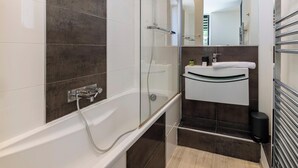 Ein modernes Badezimmer mit einer gläsernen Duschkabine, einer weißen Badewanne und einem dunklen Fliesenwaschtisch.