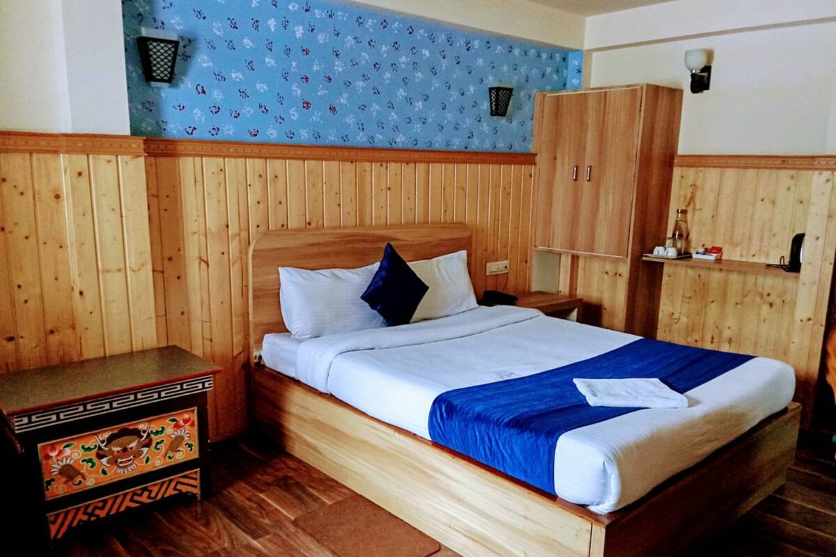 A wooden bed with white and blue bedding, a wooden nightstand, a wooden wardrobe, and a blue floral wall.