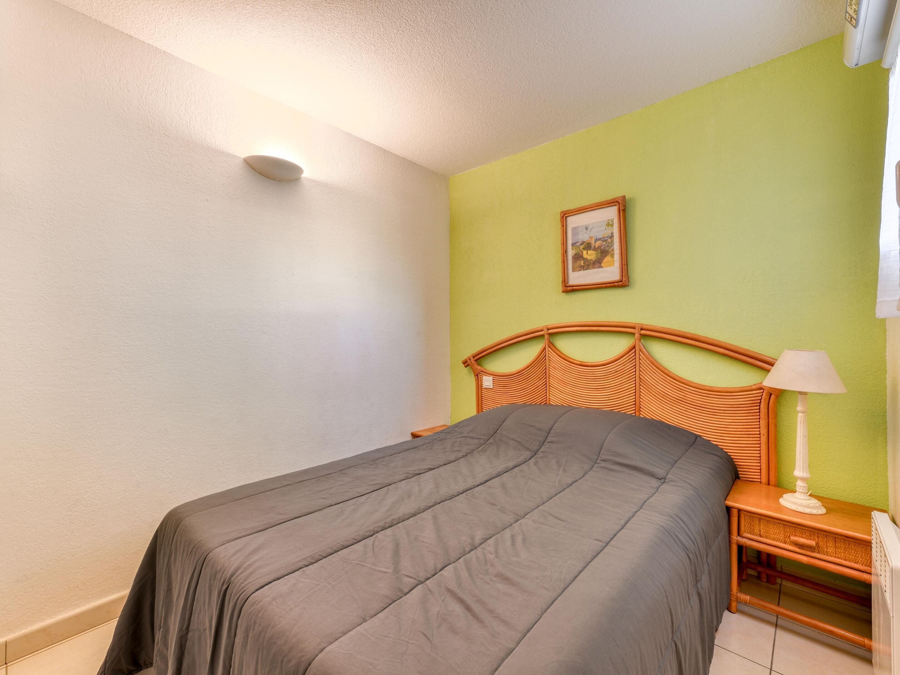 A room with a bed, a nightstand, a lamp, and a picture on the wall.