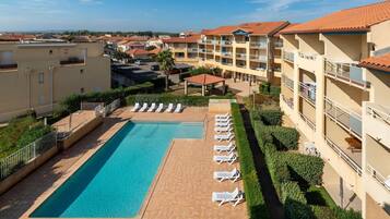 A hotel with a swimming pool, lounge chairs, and a view of the surrounding buildings.